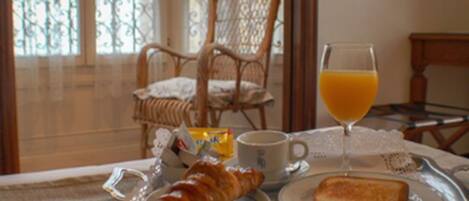 A breakfast tray with croissant, toast, and orange juice on a table with a wicker chair in the background.