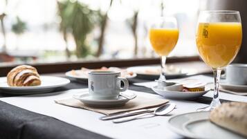 Un desayuno con croissants, una taza, un vaso de jugo de naranja y un vaso de leche sobre una mesa.