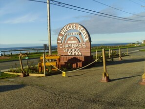 A wooden sign for the "Chambres Studios Suites" with a view of the ocean in the background.