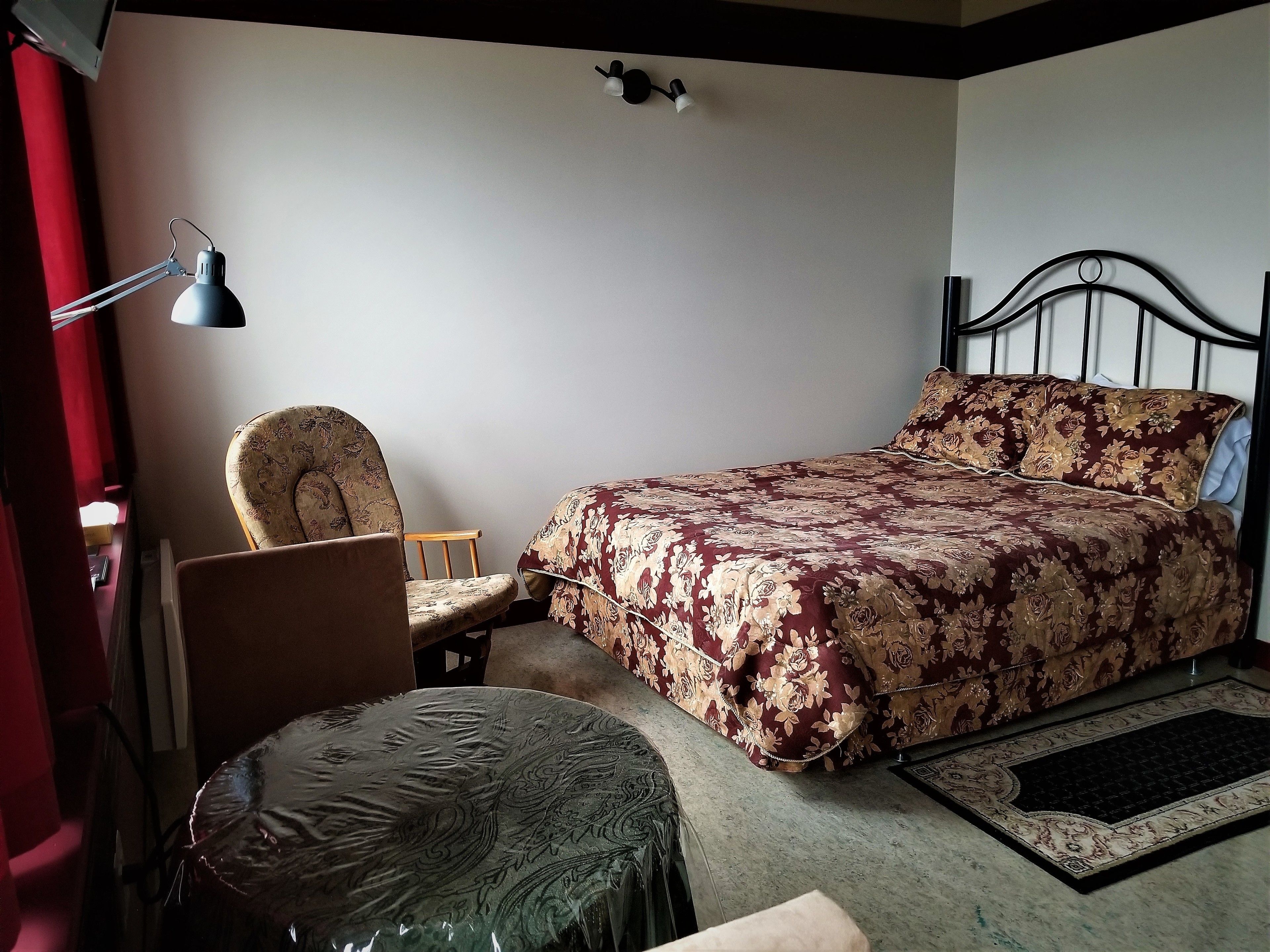 A bedroom with a bed, a chair, a desk, and a desk lamp.