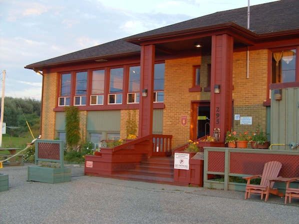 A red brick building with a staircase leading to the entrance, a sign indicating no parking, and outdoor seating with chairs.