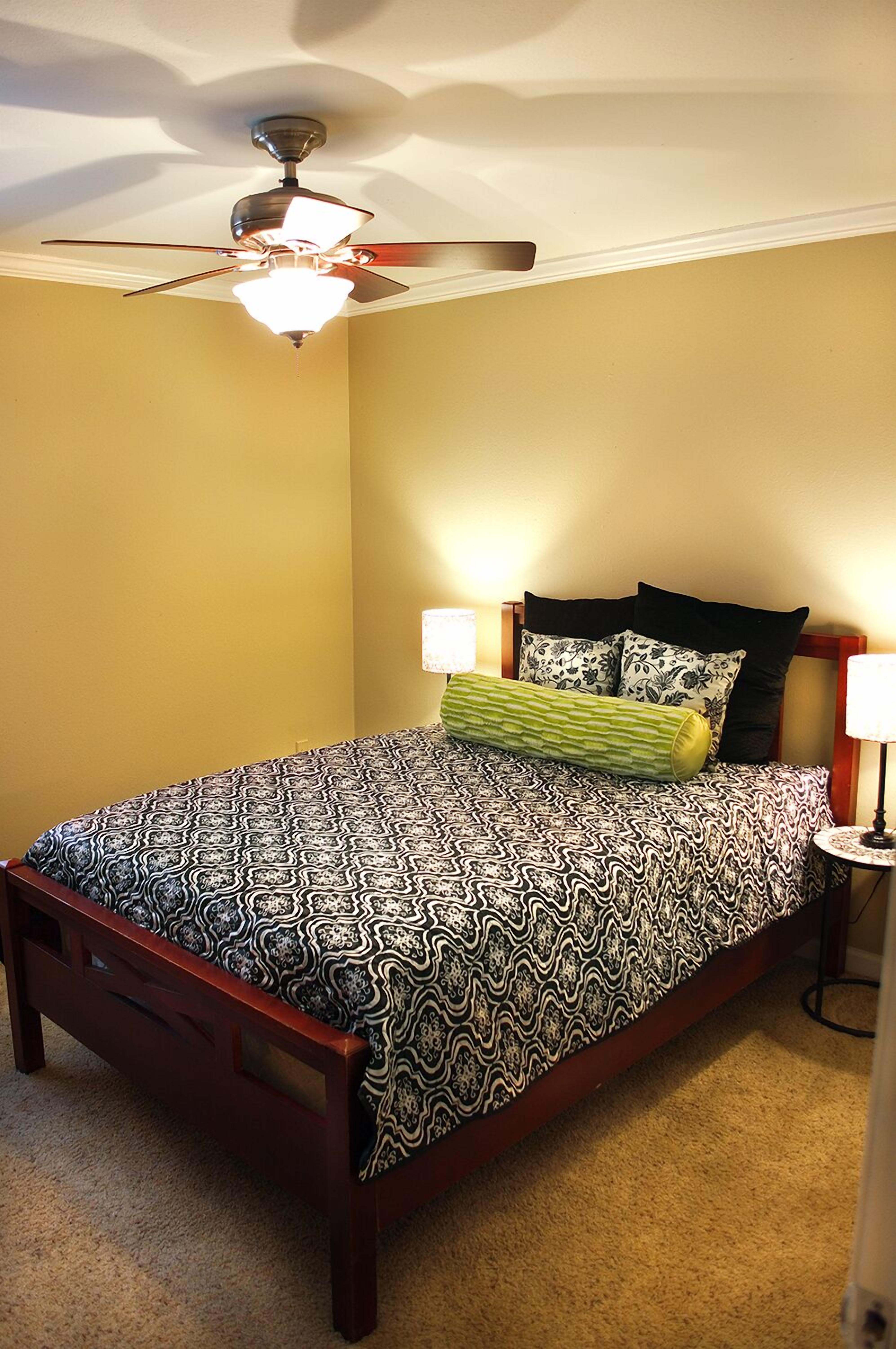 A bedroom with a bed, a ceiling fan, two bedside lamps, and a nightstand.