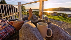 Eine Person entspannt sich auf einem Balkon mit Blick auf einen See und Hügel.