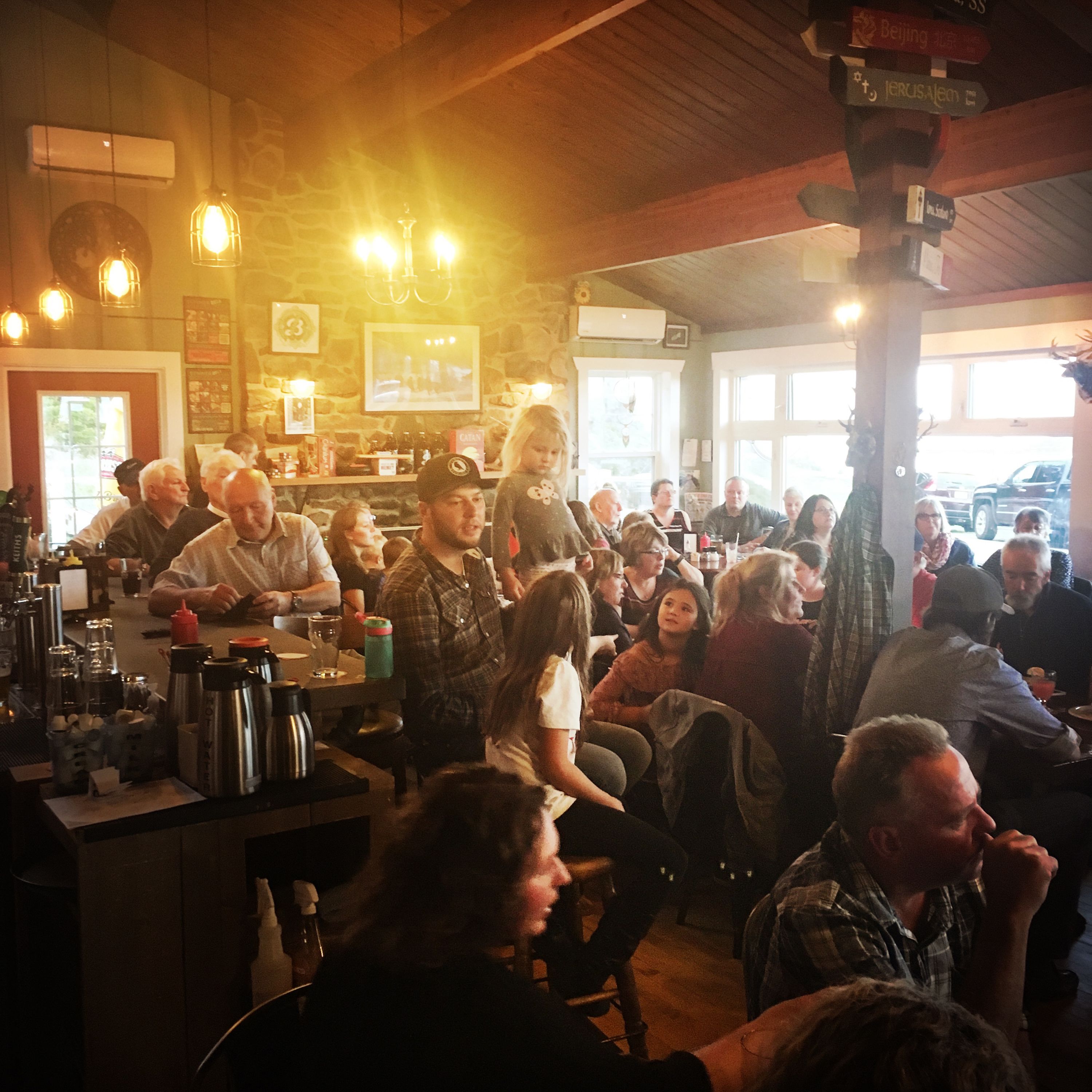 Een bruisende bar met gasten aan tafels, een houten plafond en een stenen muur.