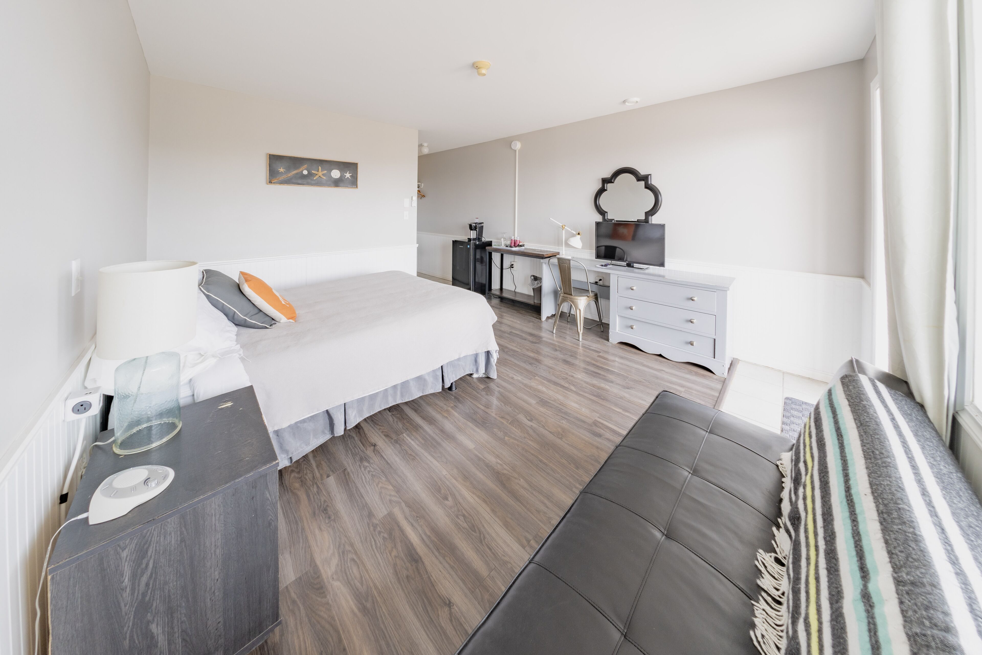 Ein modernes Hotelzimmer mit einem großen Bett, einem Schreibtisch, einem Stuhl und einer kleinen Küchenzeile.