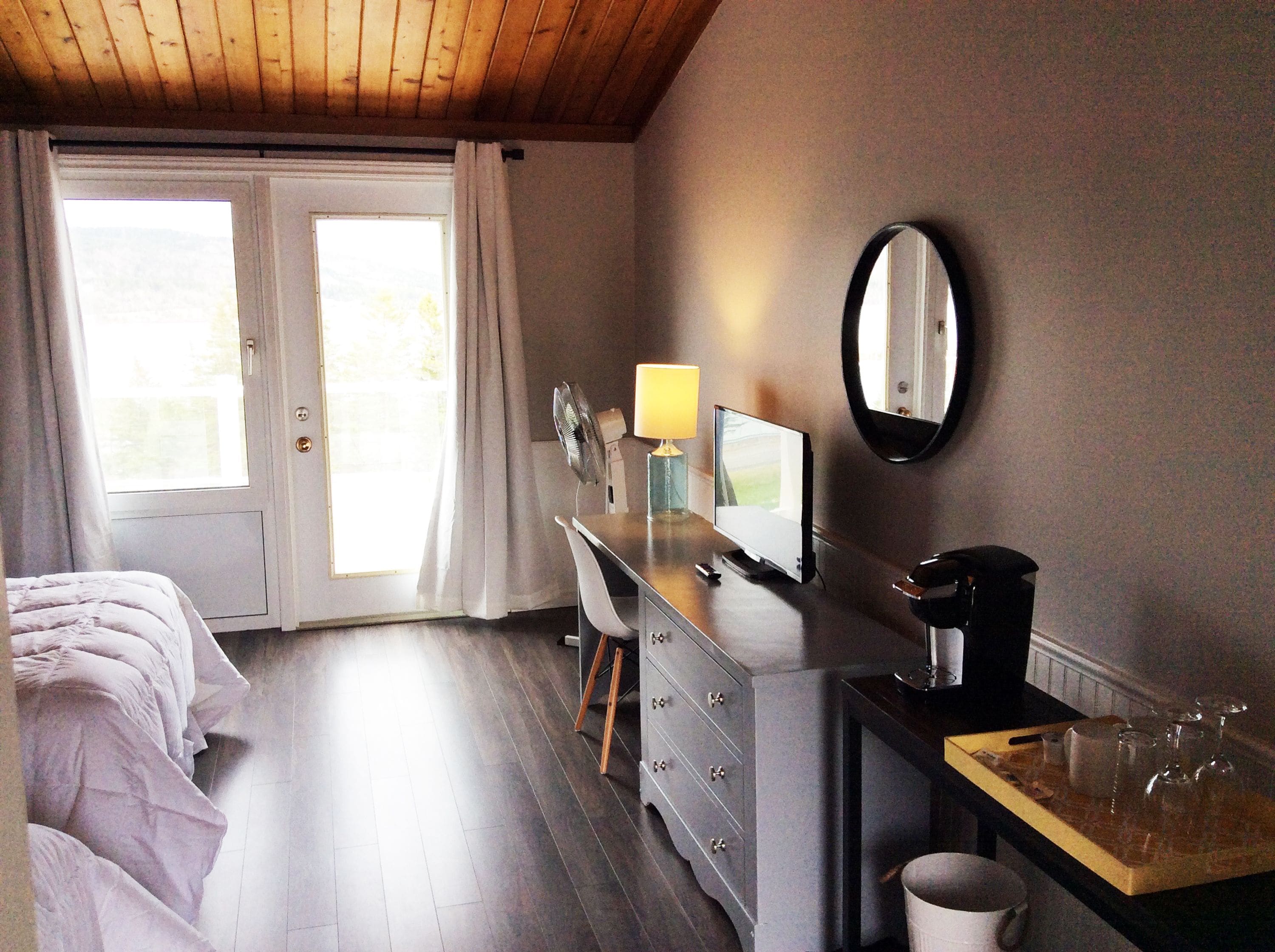 Une chambre à coucher comprenant un lit, une commode, un bureau avec une lampe, une télévision et un miroir.