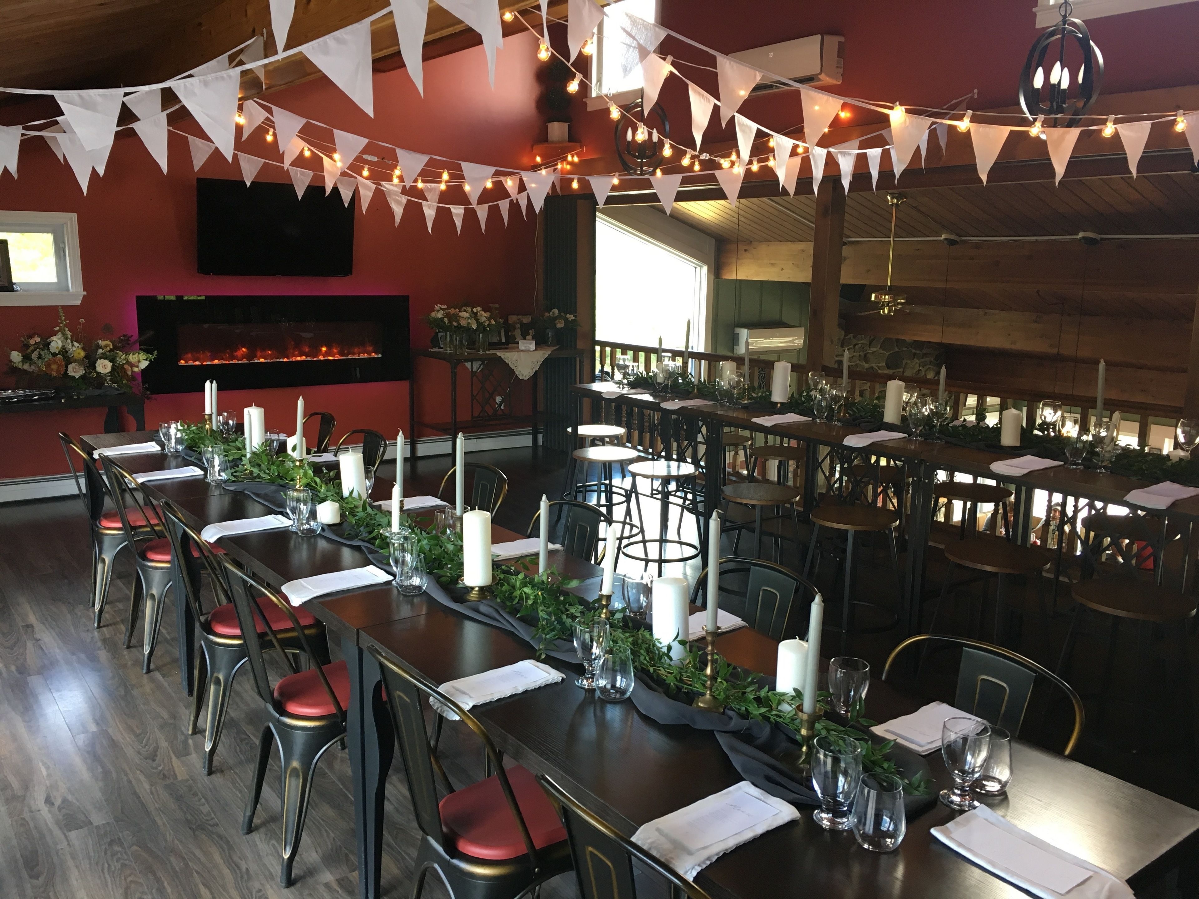 Un restaurante con largas mesas dispuestas para cenar, con velas blancas, cristalería y plantas.