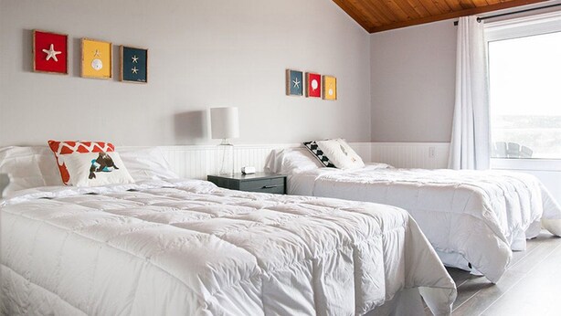 Ein Hotelzimmer mit zwei Betten, weißer Bettwäsche, einer Holzbalkendecke und Bildern an den Wänden.