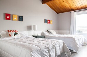A hotel room with two beds, white bedding, a wooden ceiling, and artwork on the walls. - The Iona Heights Inn (Iona)