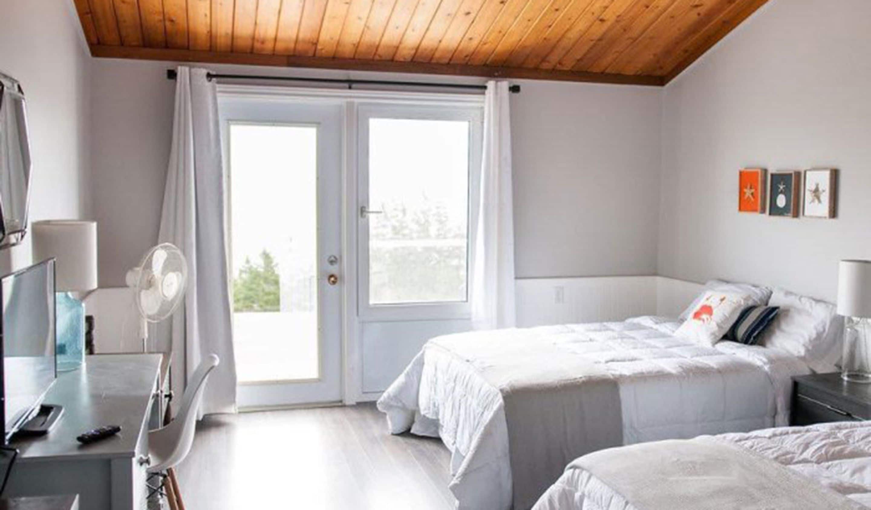 Un dormitorio con cama, escritorio, silla, ventilador y ventana con cortinas.