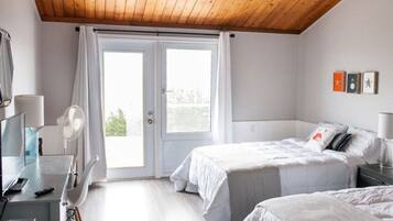 Un dormitorio con cama, escritorio, silla, ventilador y ventana con cortinas.