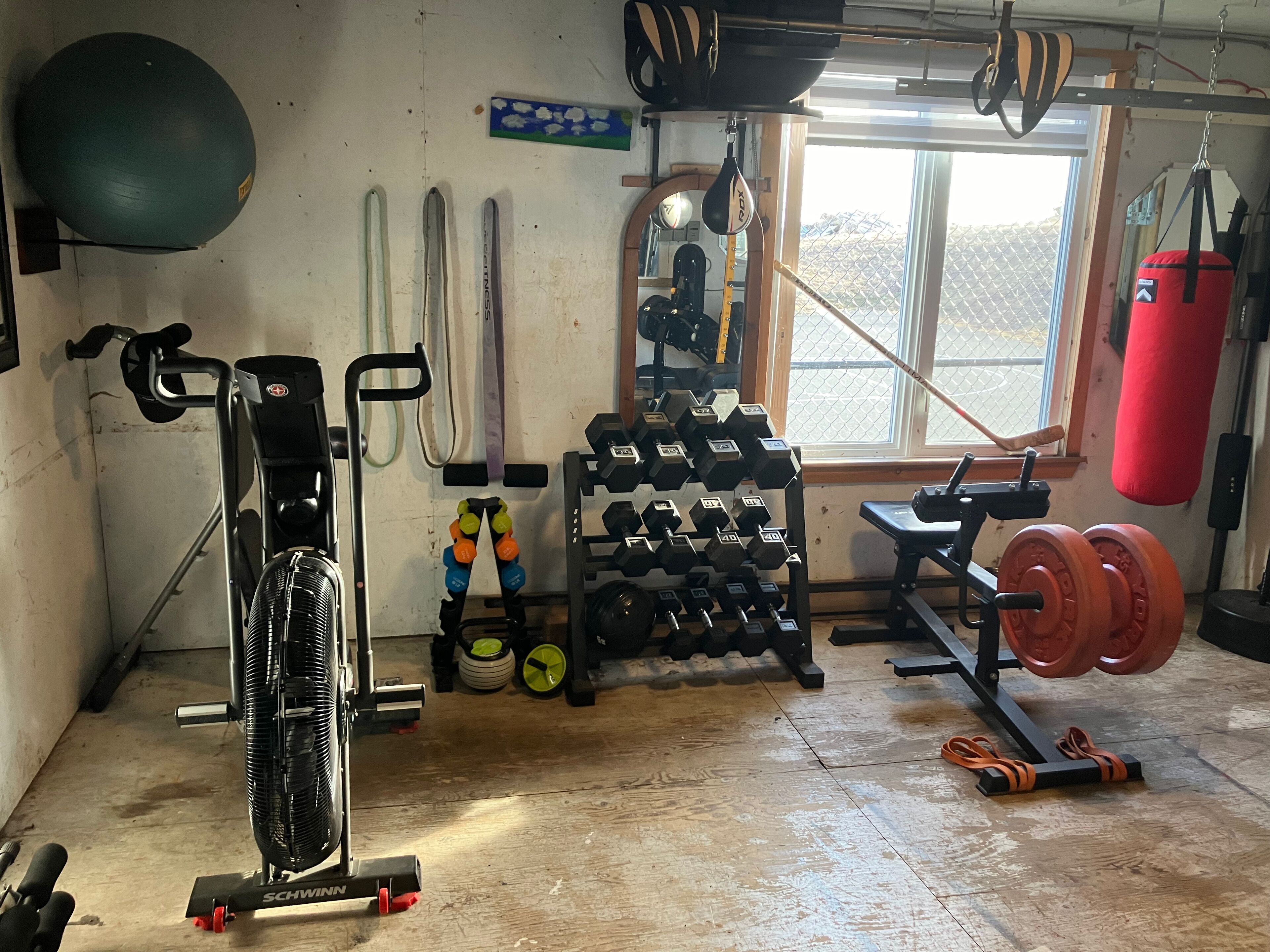 Un gimnasio en casa con equipo de ejercicio, incluyendo una bicicleta estática, mancuernas, kettlebells y un saco de boxeo.