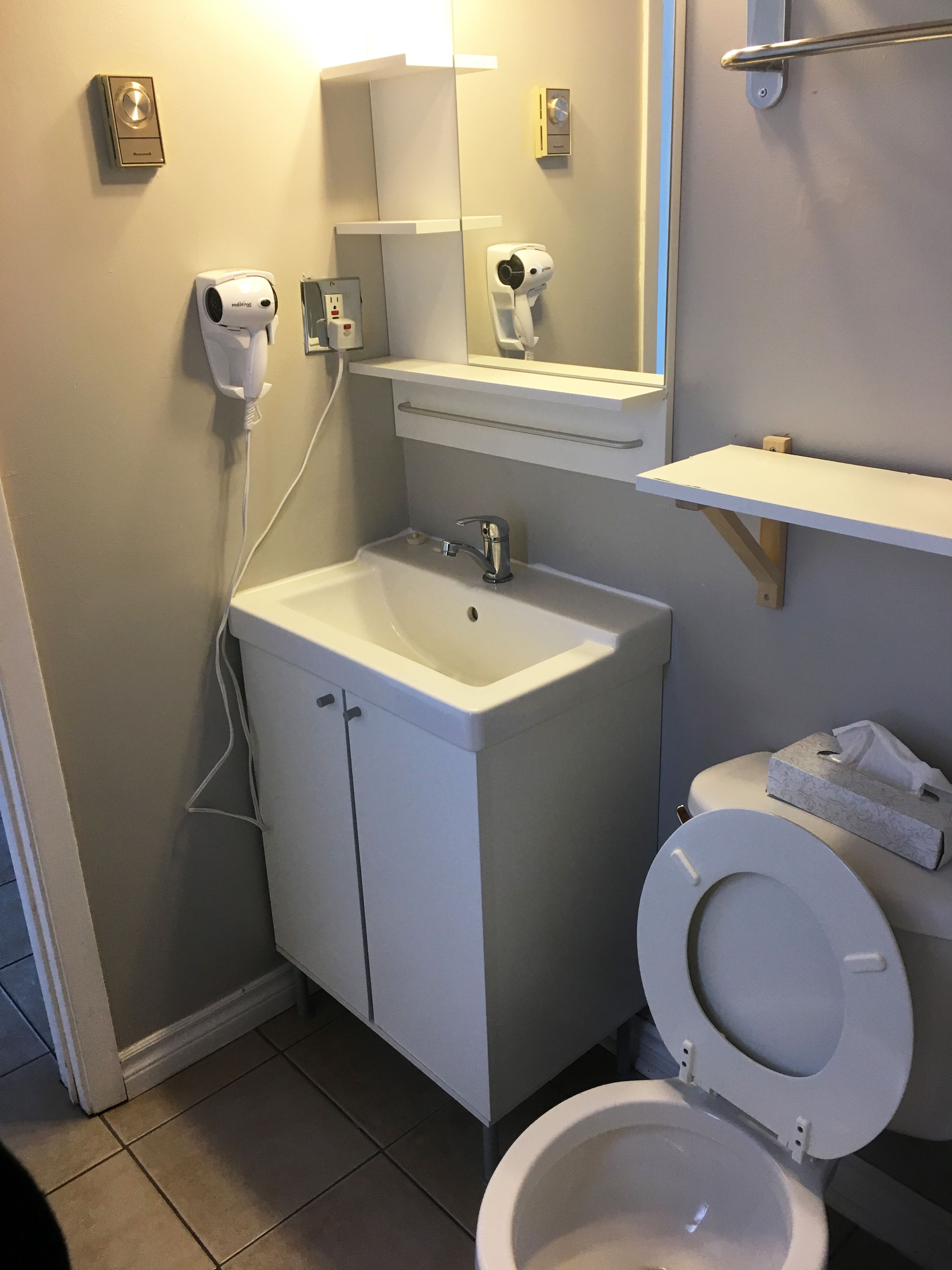 Un baño con lavamanos blanco, un espejo, inodoro y dispensador de toallas.