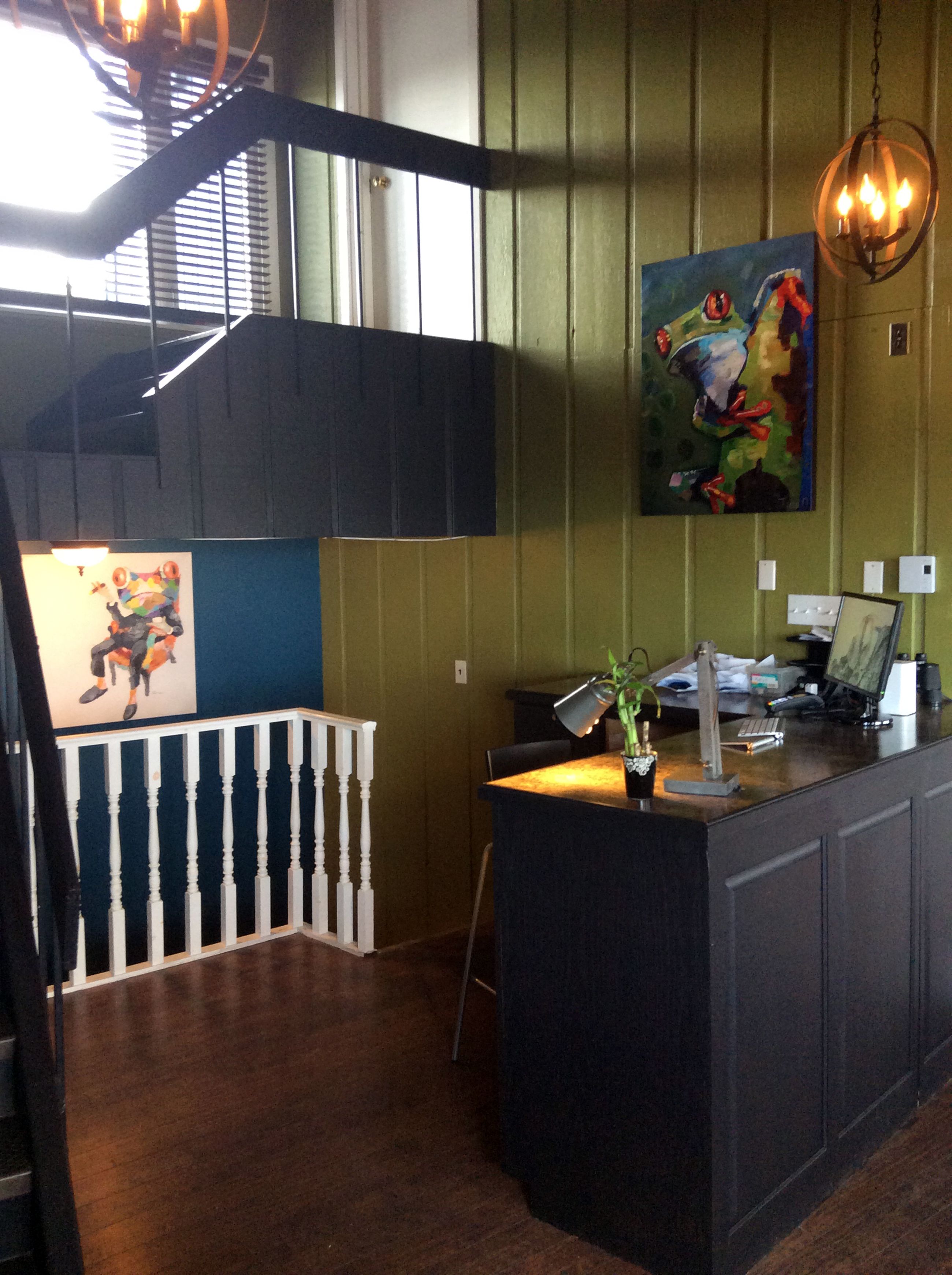 A reception area with a desk, a computer, and a painting on the wall.