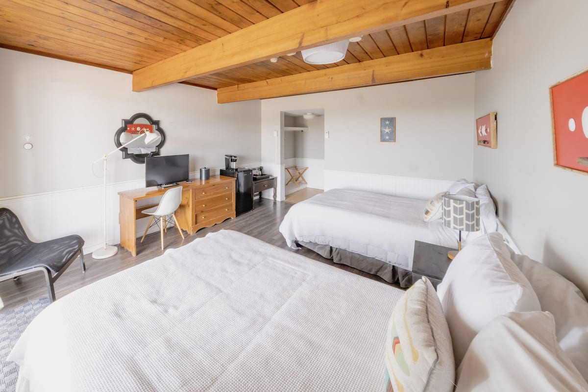 Ein Schlafzimmer mit zwei Betten, einem Schreibtisch, einem Stuhl, einem Fernseher und einer Kaffeemaschine.