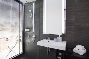 Un bagno moderno con una grande finestra, un lavandino bianco, uno specchio e una doccia.
