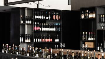 A modern bar with black leather seating and wooden tables, featuring a wine rack with numerous bottles and glasses.