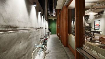 Un corredor estrecho con bicicletas estacionadas a la izquierda, una puerta verde al fondo y una zona de estar con sillas y una mesa a la derecha.