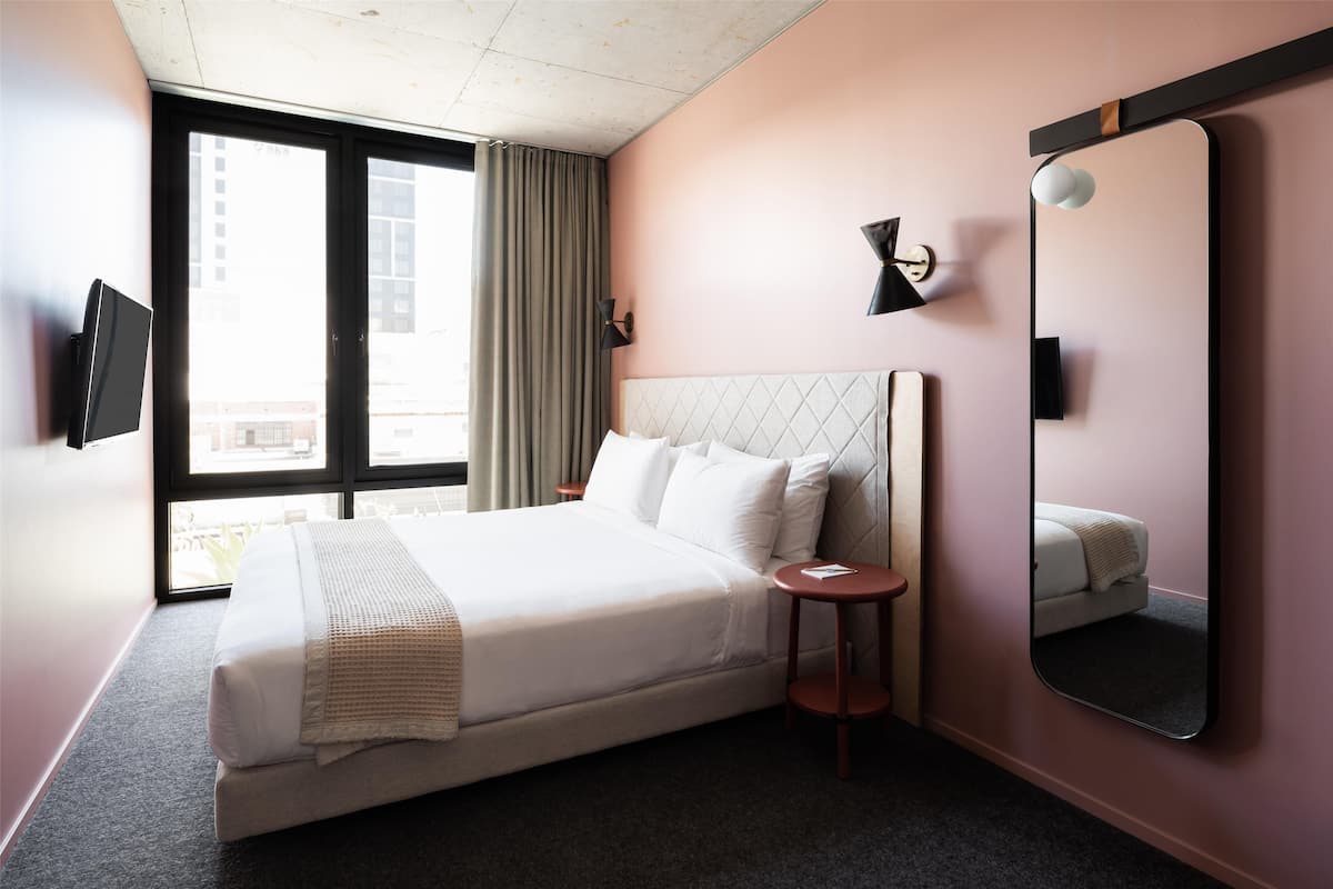 A hotel room with a large bed, a bedside table, a mirror, and a television on the wall.