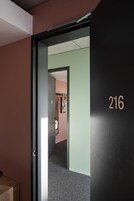 Un corridoio con una porta contrassegnata dal numero 216, pavimento in moquette e un interruttore a parete.