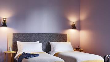 Une chambre d’hôtel avec deux lits, une tête de lit, des tables de chevet, une valise et des lampes fixées au mur.