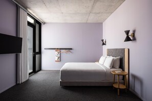 A modern hotel room with a bed, a small side table, a TV, and a window with curtains.