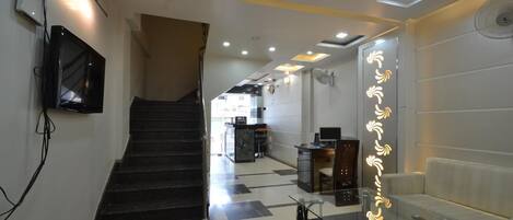 A hotel lobby with a staircase, a reception desk, a sofa, and a glass table.