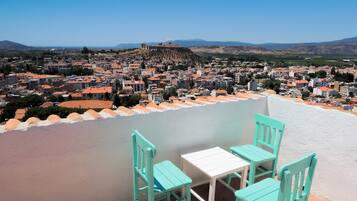 A terrace with turquoise chairs and a table overlooking a cityscape with a hill and buildings.