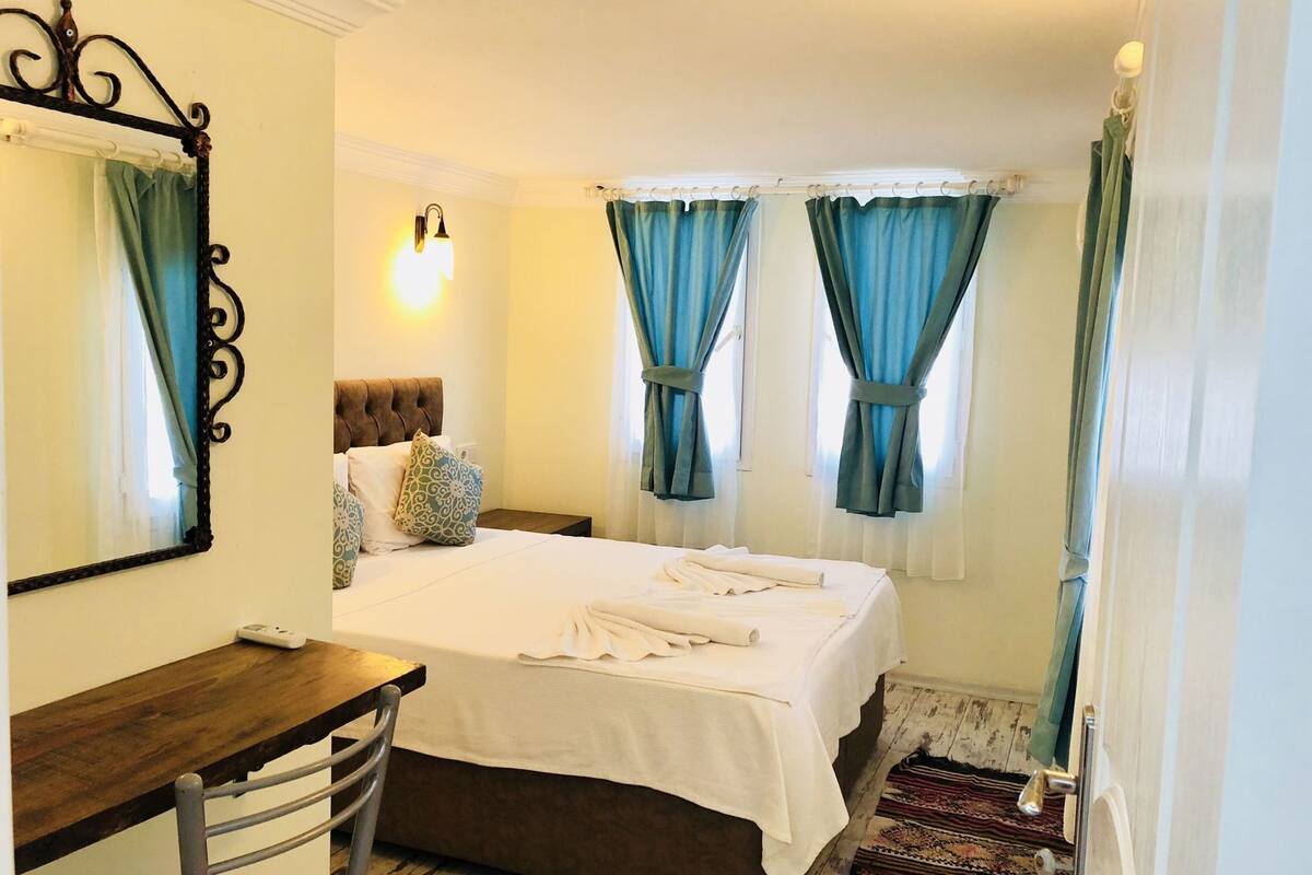 A bedroom with a bed, a desk, a chair, a mirror, and curtains.
