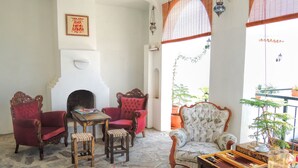 A traditional room with a stone floor, red and white upholstered chairs, a wooden table with a board game, and a white fireplace. - Villa Dreams (Selçuk)