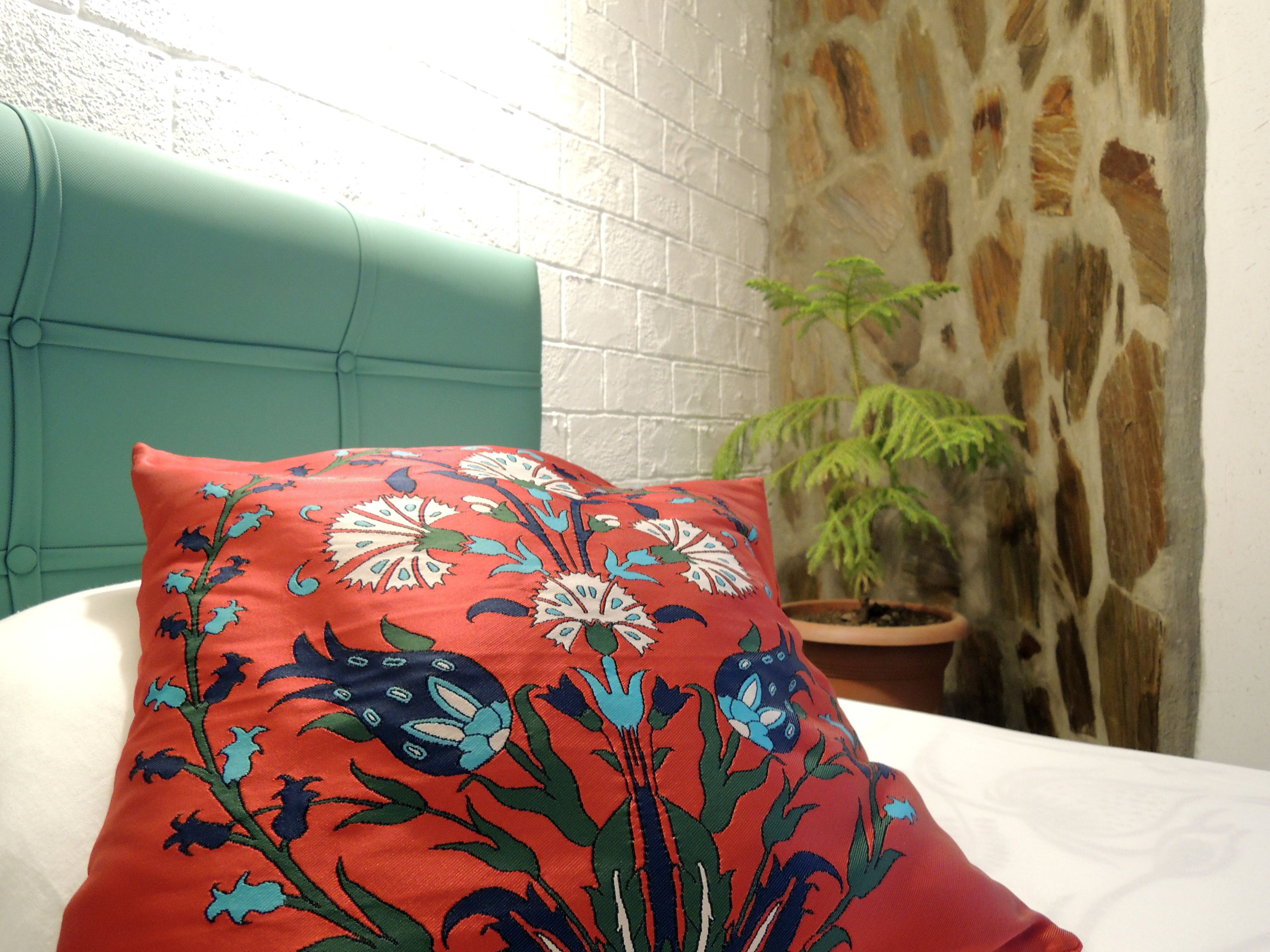 A bed with a red pillow featuring a floral pattern, a teal headboard, a white wall, and a potted plant.