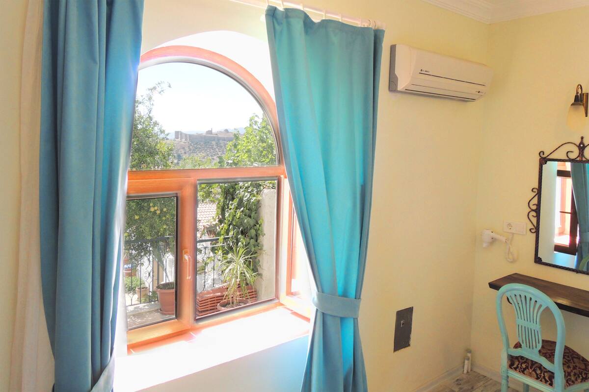 A room with a window, curtains, an air conditioner, a chair, and a mirror.