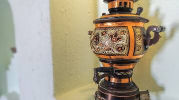 Un samovar de bronce tradicional con diseños intrincados, sobre una superficie blanca frente a una pared amarilla.