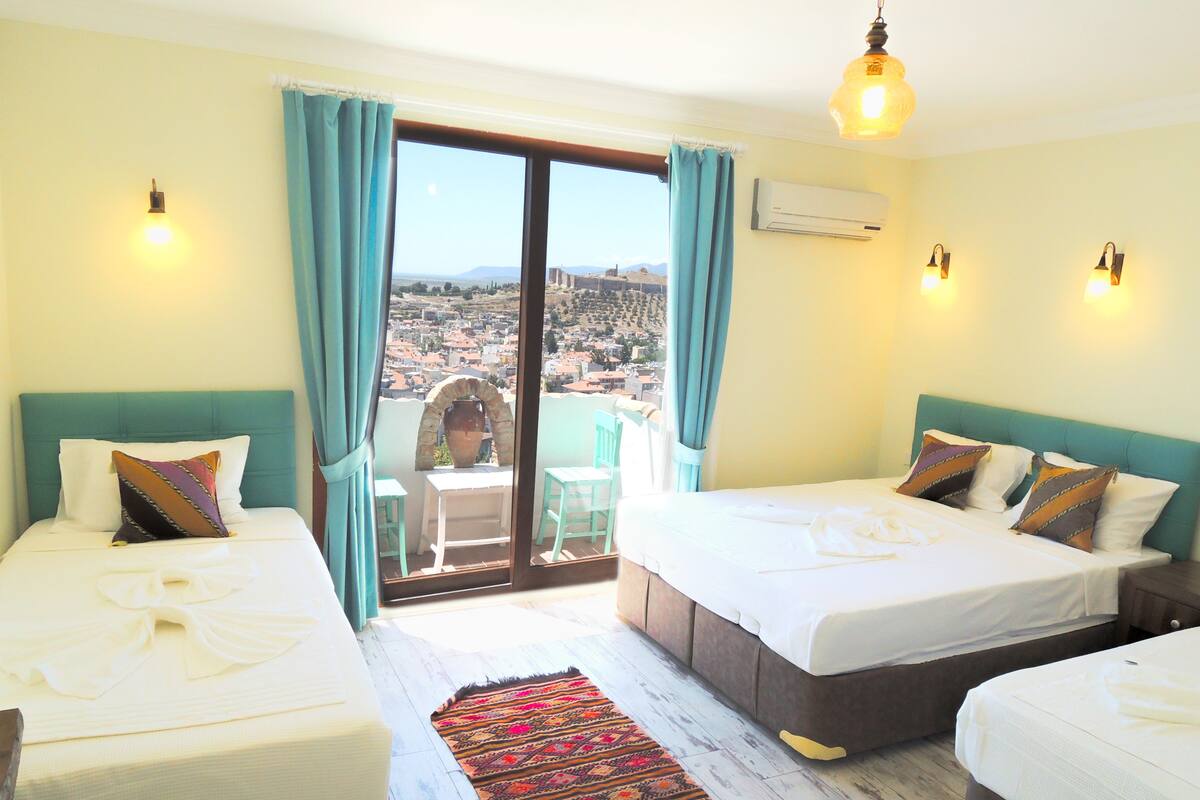 A hotel room with two beds, a view of a cityscape, a balcony with a table and chairs, and an air conditioning unit.