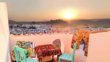 A balcony with a table and chairs, overlooking a cityscape during sunset.