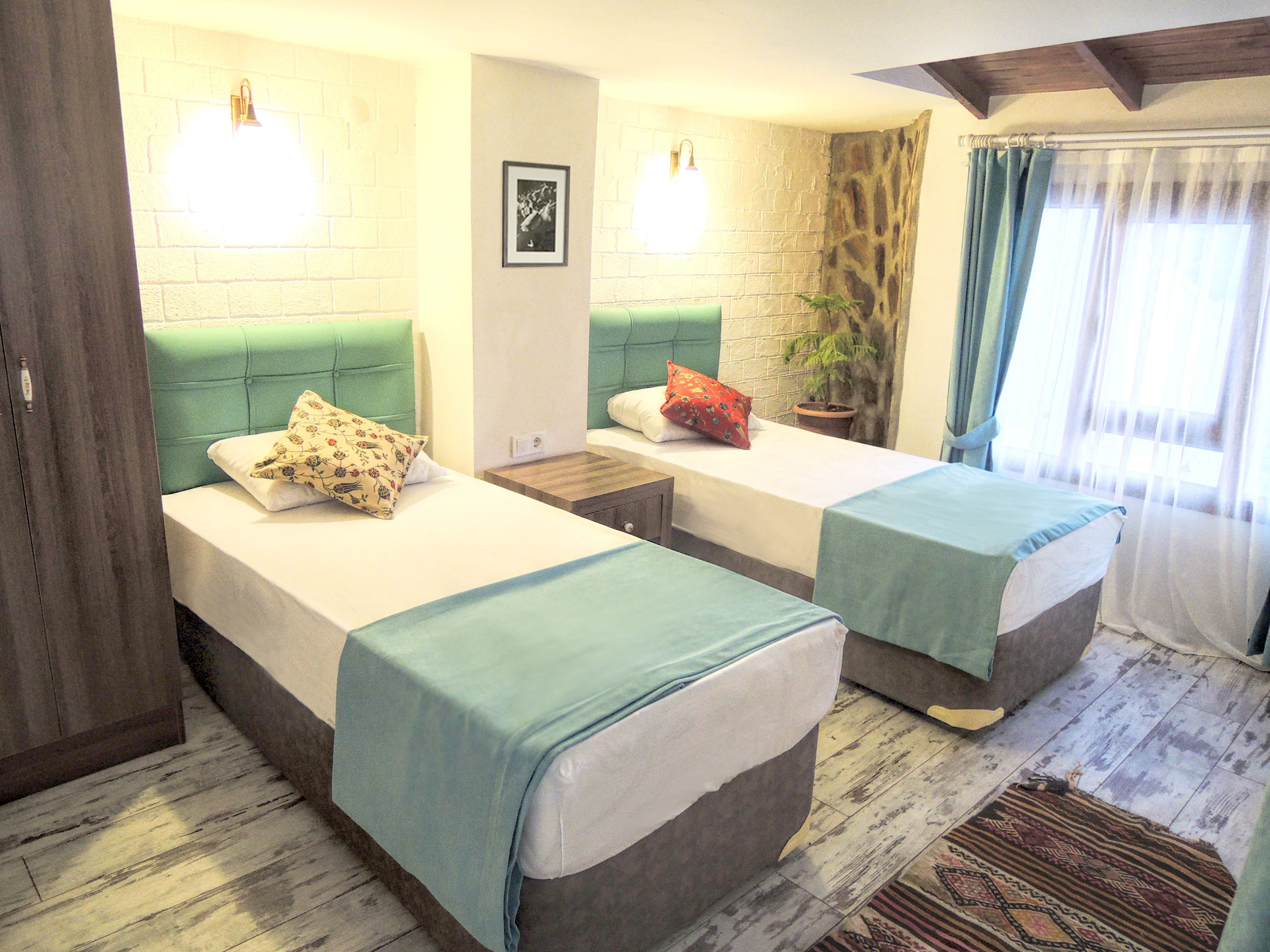 Una habitación con dos camas, cada una con cabecera verde, una mesita de noche y una planta en maceta.
