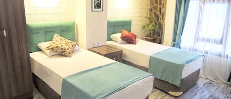Una habitación con dos camas, cada una con cabecera verde, una mesita de noche y una planta en maceta.