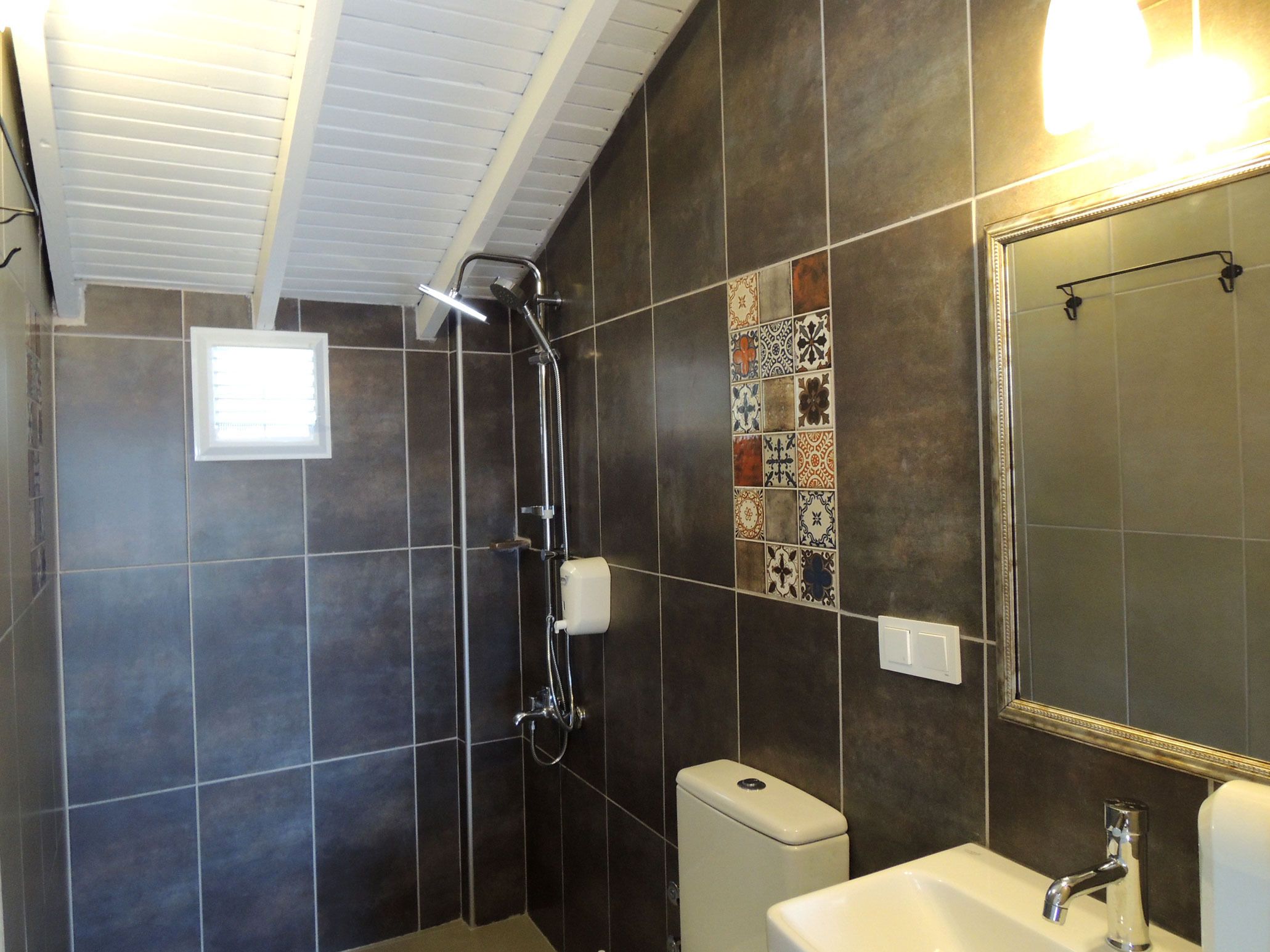 A bathroom with dark tiles, a shower, a toilet, a sink, and a mirror.