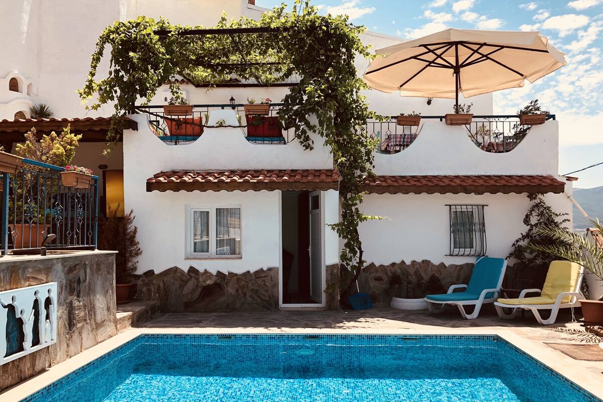A poolside area with a tiled pool, outdoor seating, and a pergola with hanging planters.