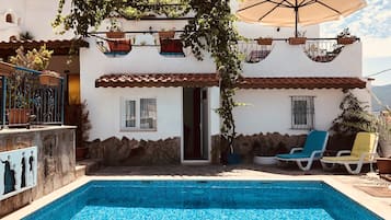 A poolside area with a tiled pool, outdoor seating, and a pergola with hanging planters.
