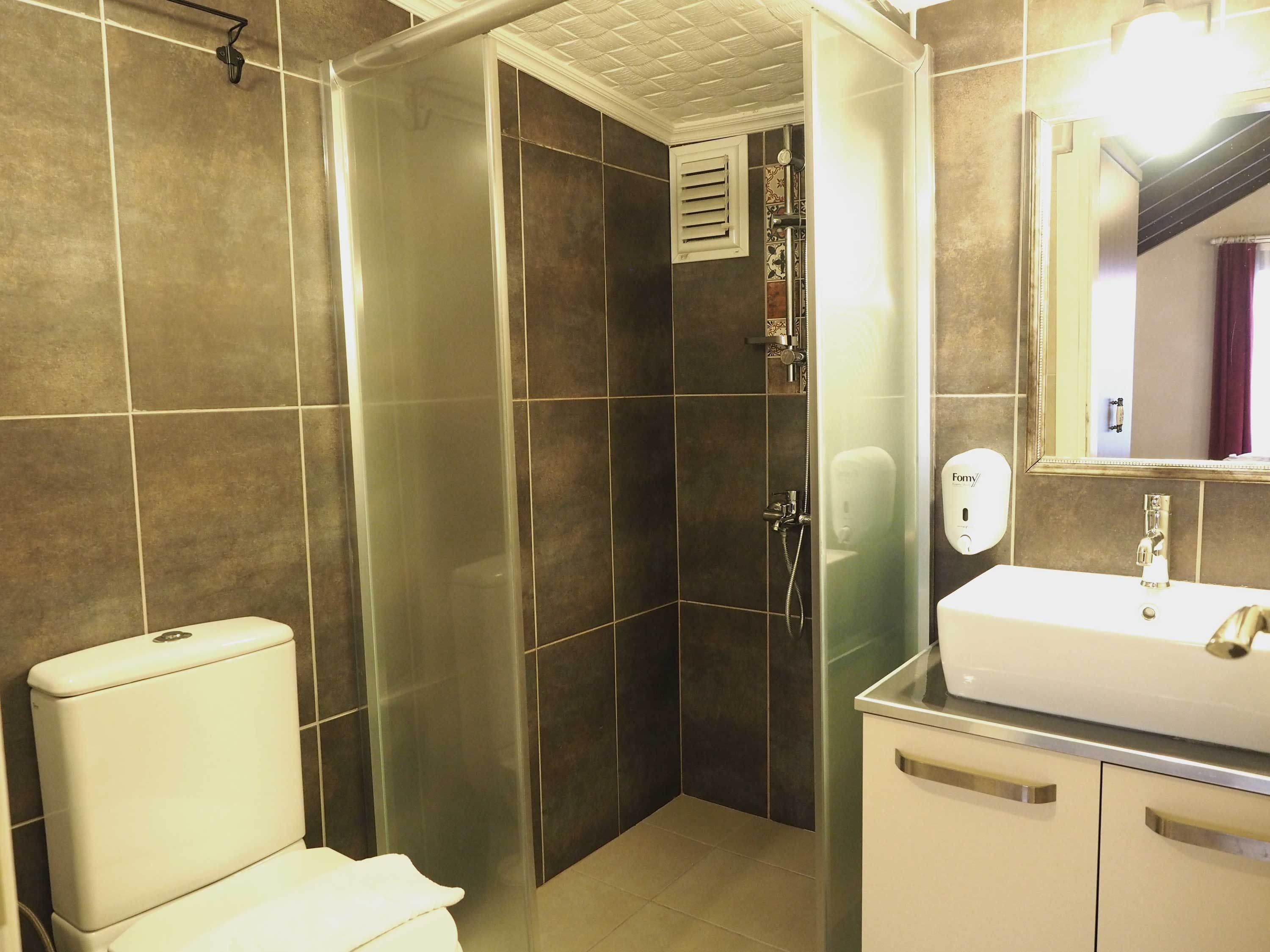 Un baño con inodoro, ducha con puerta de vidrio, lavabo y espejo.