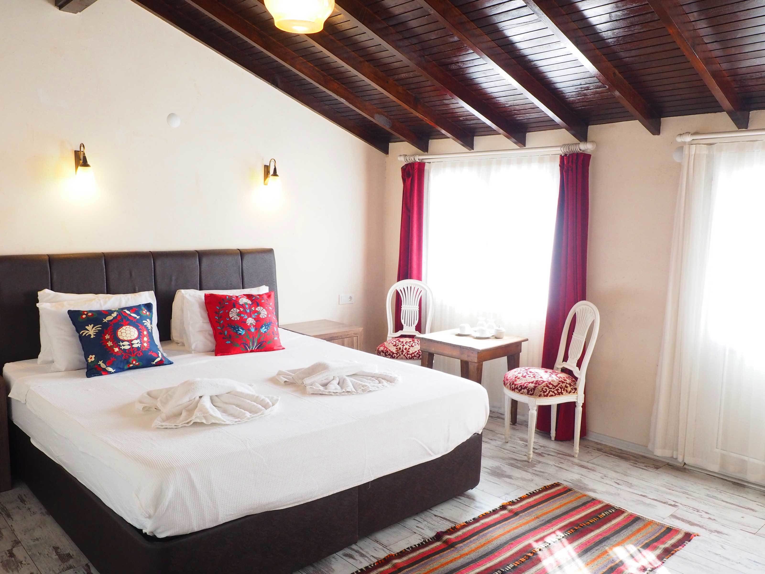 A hotel room with a large bed, two bedside tables, a small table, two chairs, and a window with curtains.