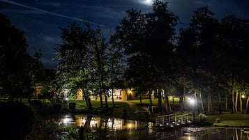 A nighttime park scene with a pond, trees, and a building with lights.