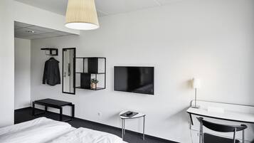 Una habitación de hotel moderna con una cama, un escritorio con una silla, un televisor, un espejo y una lámpara colgante.