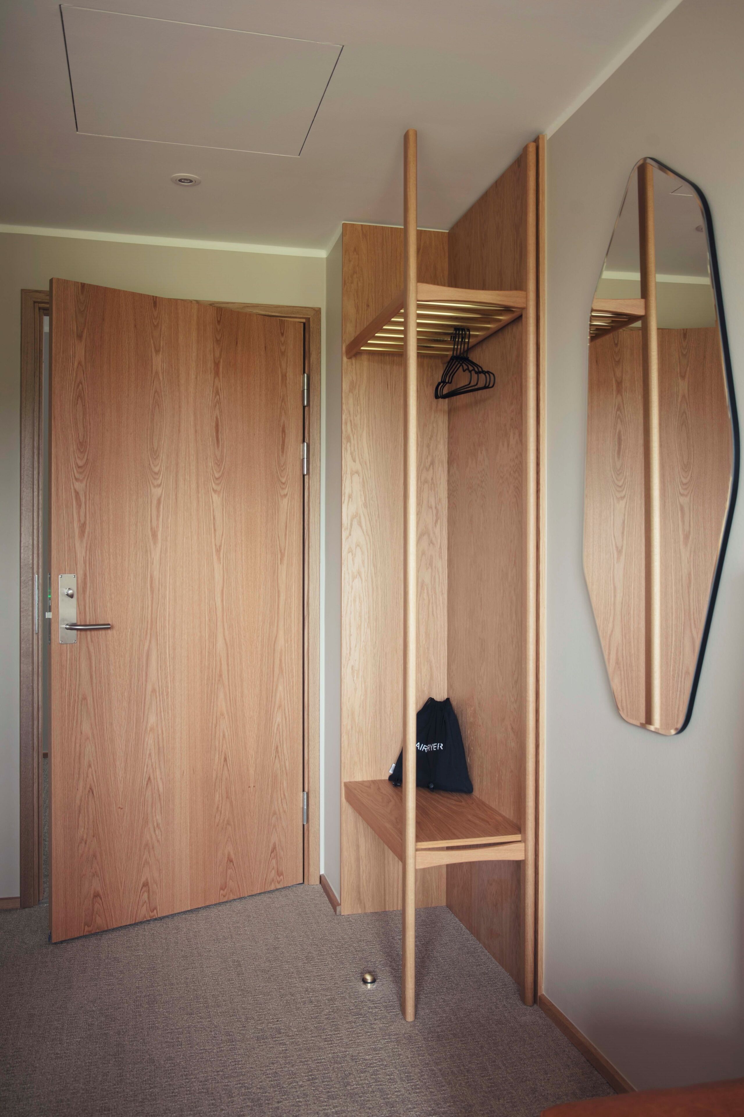 A room with a wooden wardrobe, a mirror, and a shelf with a bag.