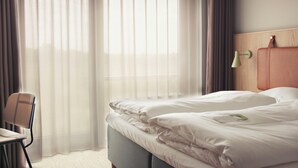 Una habitación de hotel con cama, una silla, una lámpara y ventana con cortinas.
