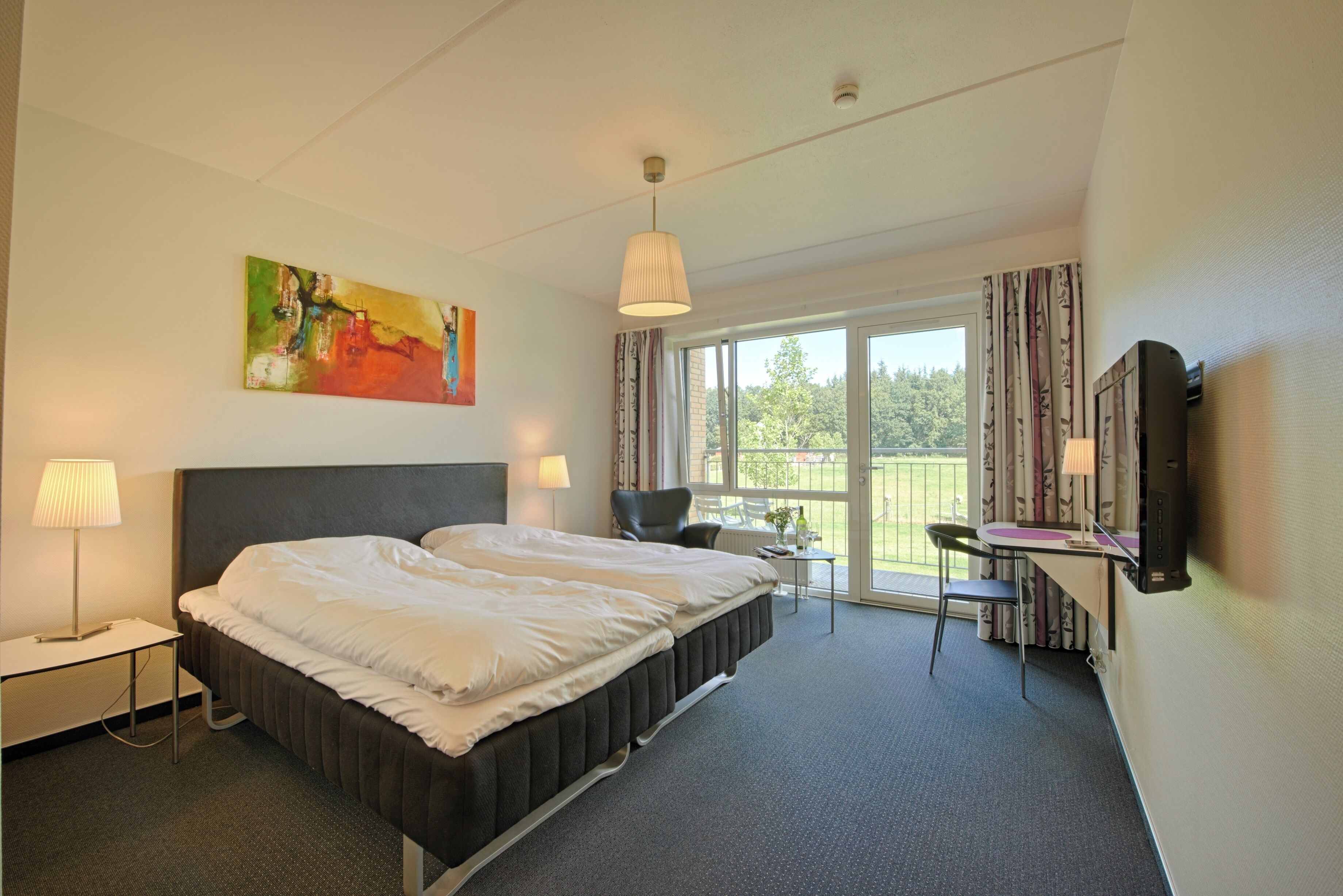 A hotel room with a large bed, a desk, a chair, a TV, and a painting on the wall.