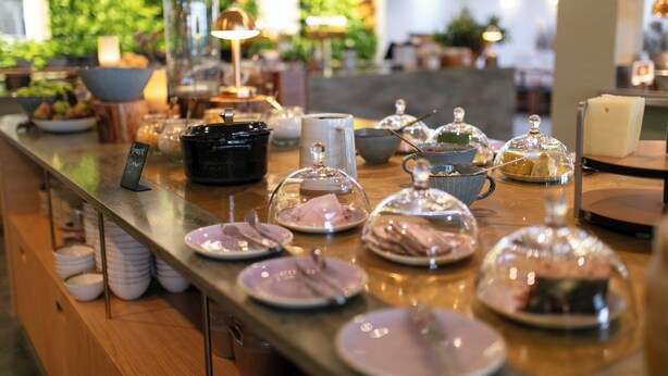 Montaje de buffet con diversos platos y condimentos, una estación de café y una pared verde de fondo.