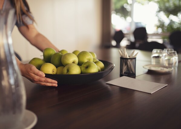 A person holding a bowl of green apples on a wooden table with a glass of water, a notepad, and a pen holder. - Fjelsted Skov Hotel & Konference (Middelfart)