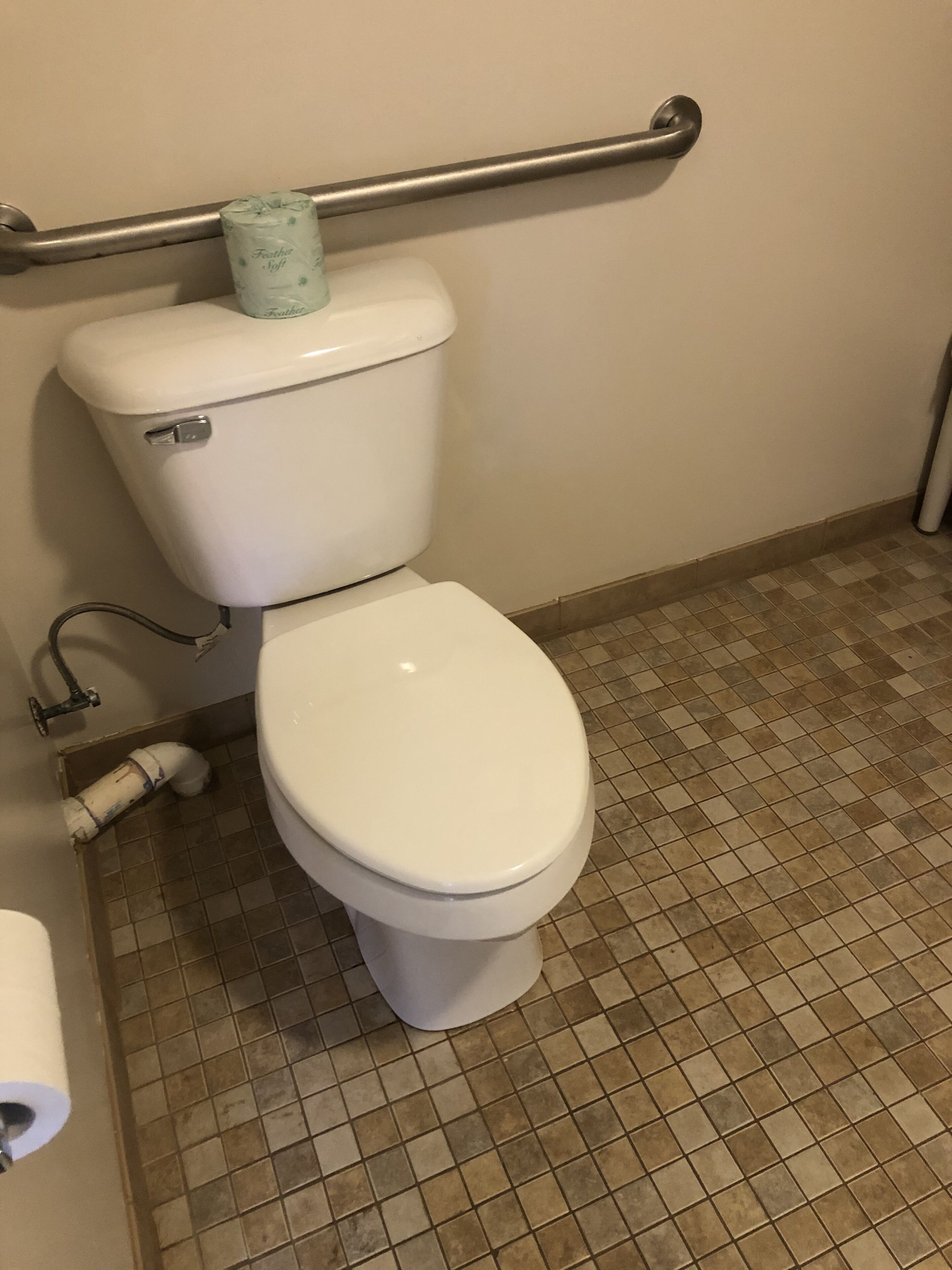 Lavabo blanc amb un rotlle de paper higiènic al dipòsit, una barana d'agafa a la paret i un sòl de rajoles.